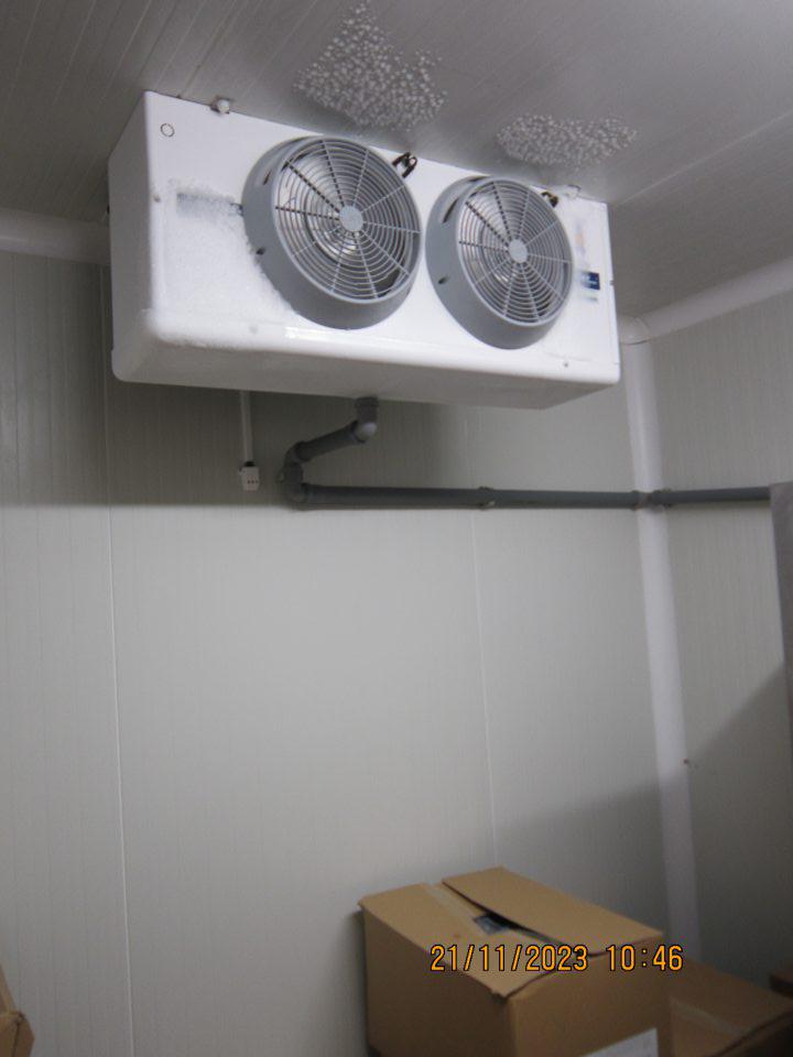 Nadmerná námraza v mraziacom boxe v zázemí prevádzky na mraziacej jednotke a strope, pod ktorými sú uložené otvorené kartónové krabice s mrazenými pekárskymi výrobkami určenými k dopekaniu.