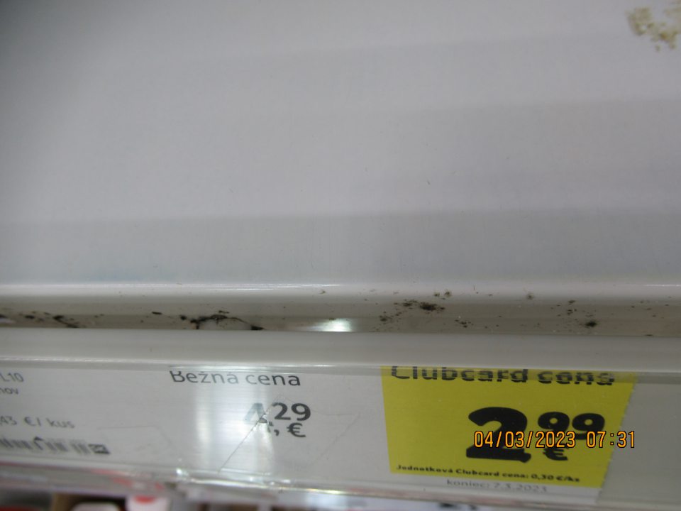 V drážke medzi regálom a cenovkou na regáloch na mliečne výrobky čierne znečistenie.