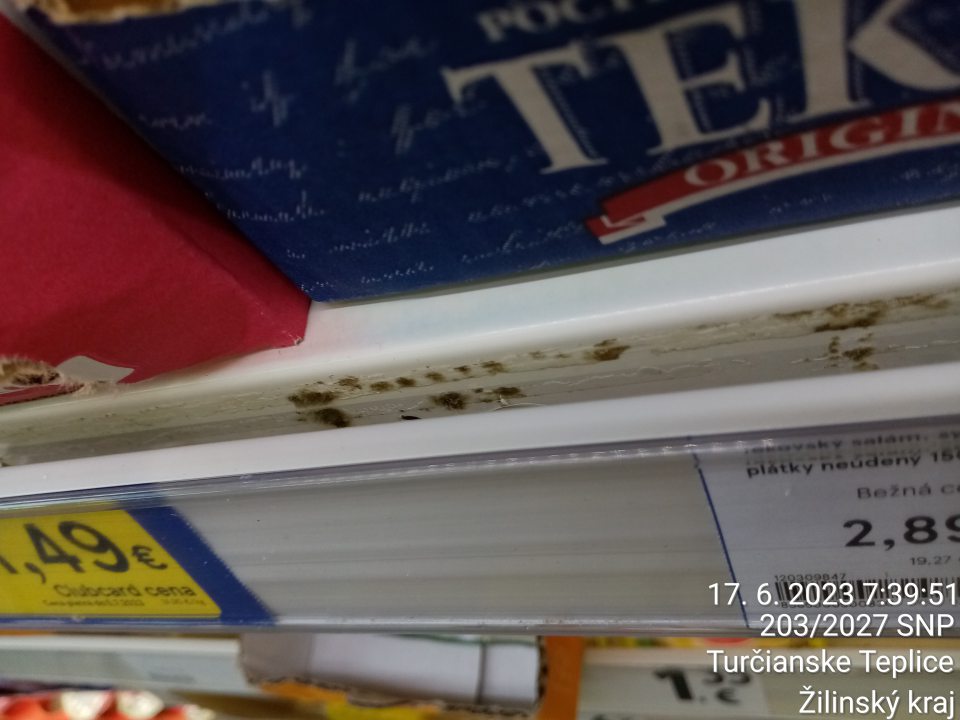 Znečistenie čiernymi nečistotami podobnými plesni regálov v prednej časti pod lištou na cenovky pri predaji tekovského salámového syra.