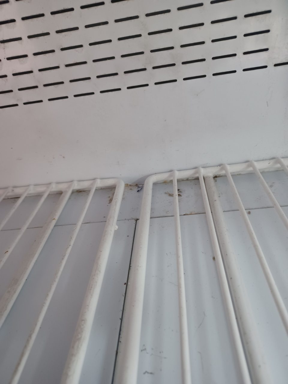 Znečistený priestor v chladiacej vitríne na mäsové výrobky pod mriežkou na predajnej ploche.