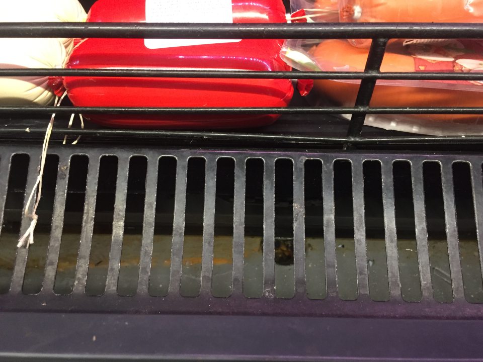 Kovová  mriežka a priestor pod mriežkou v  chladiacom zariadení  na vystavovanie a predaj mäsových výrobkov znečistená prachom, zaschnutou tekutinou.