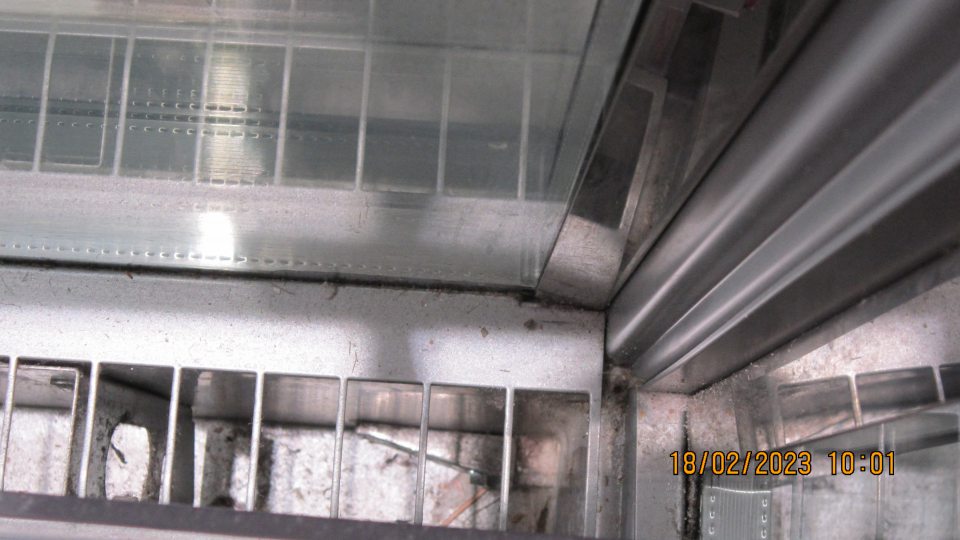 Na predajnej ploche v časti predaja mliečnych výrobkov v otvorenom chladiacom zariadení znečistený priestor pod mriežkou a kovová konštrukcia mriežky prachom, zaschnutou špinou a napadanými nečistotami.