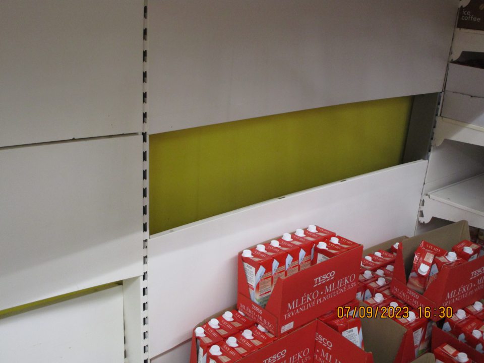 na predajnej ploche vľavo od palety s trvanlivým mliekom odtrhanuté kovové lišty, pod nimi znečistená podlaha kúskami omietky a špagátov