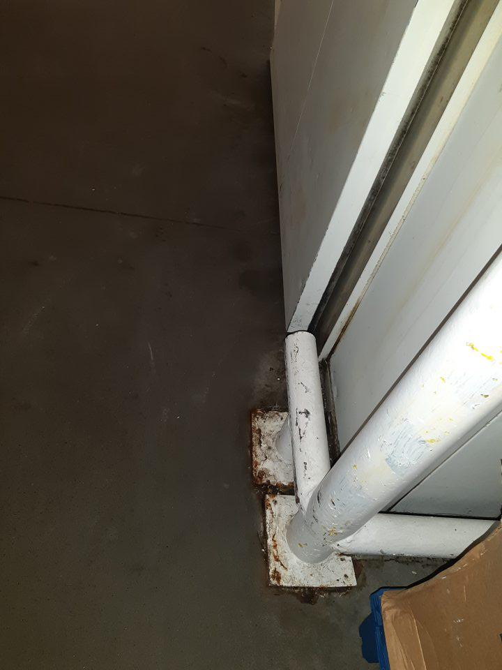 V sklade potravín kovové zábrany na podlahe majú opotrebovaný náter so známkami korózie a okolie je znečistené hrubou nečistotou.