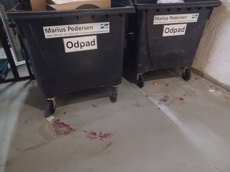 Znečistená, zatečená podlaha pod kontajnermi na odpad.