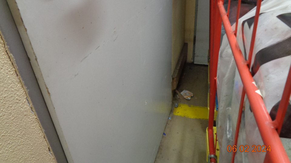 Znečistená podlaha čiernou špinou, prachom, kúskami papierov a dreva v sklade v časti uloženia vratných obalov.