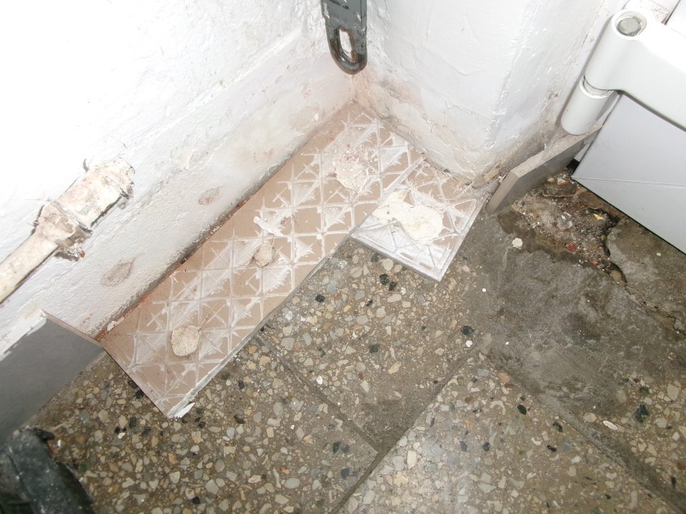 poškodená podlaha a opadávajúci sa obklad (sokel) pri vstupných dverách skladu