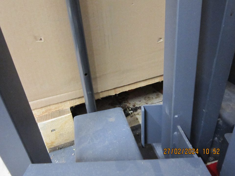 Znečistená podlaha prachom, nánosmi zaschnutej čiernej špiny, kúskami kartóna a rôznymi organickými nečistotami pri vstupných dverách do skladovacích priestorov.