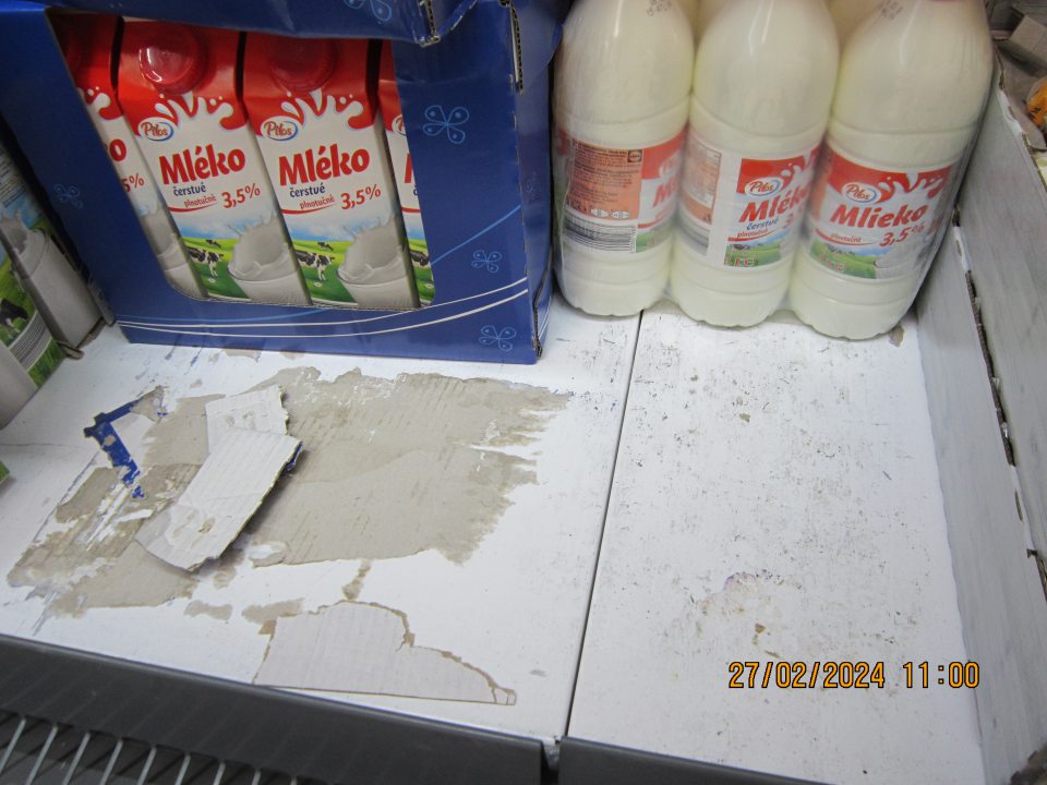Znečistený regál v chladiacej vitríne na uchovávanie čerstvého mlieka na predajnej ploche - zaschnuté nečistoty, prilepené kúsky kartónového papiera.
