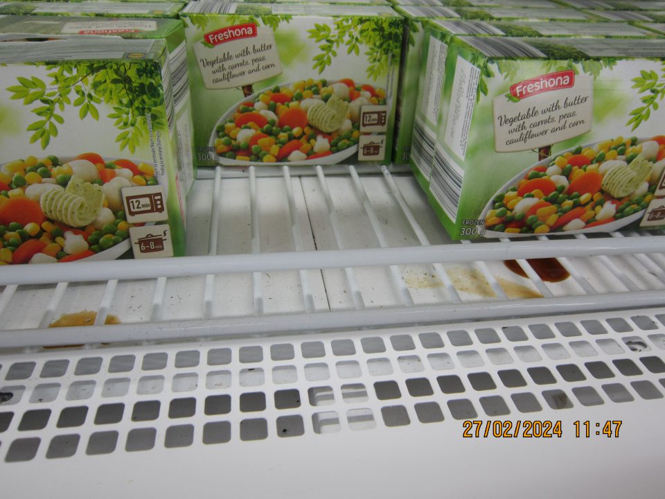 Namrznutý vytečený obsah uchovávaných potravín na dne mraziacej vitríny pre hlbokozmrazenú zeleninu na predajnej ploche.