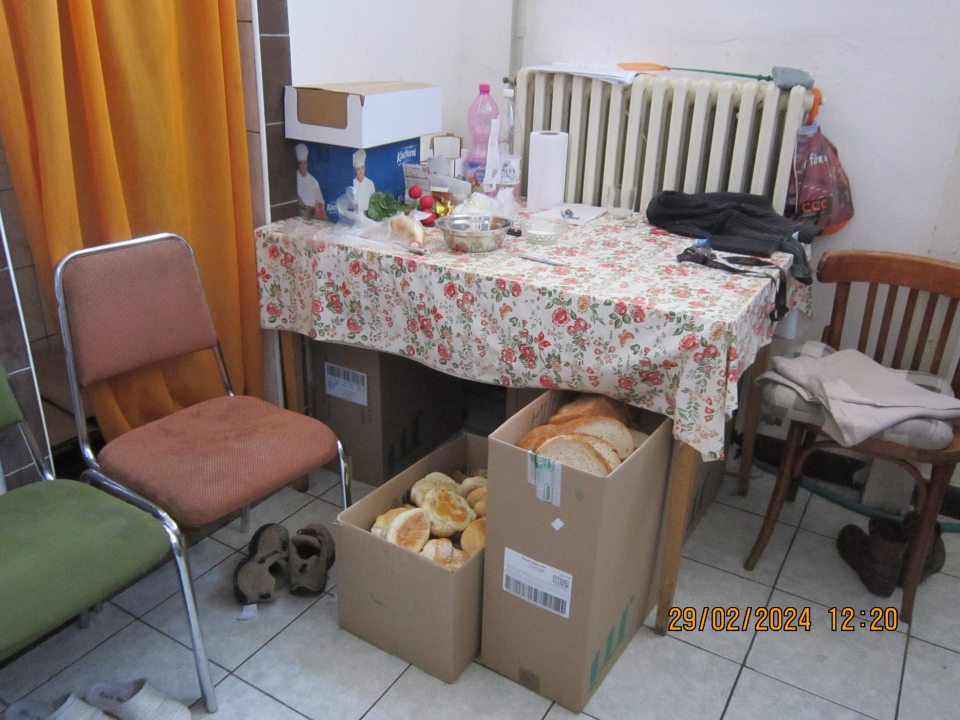 Kartónové krabice so starým pečivom vyradeným z predaja uložené pod stolom v priestoroch šatne pre zamestnancov.