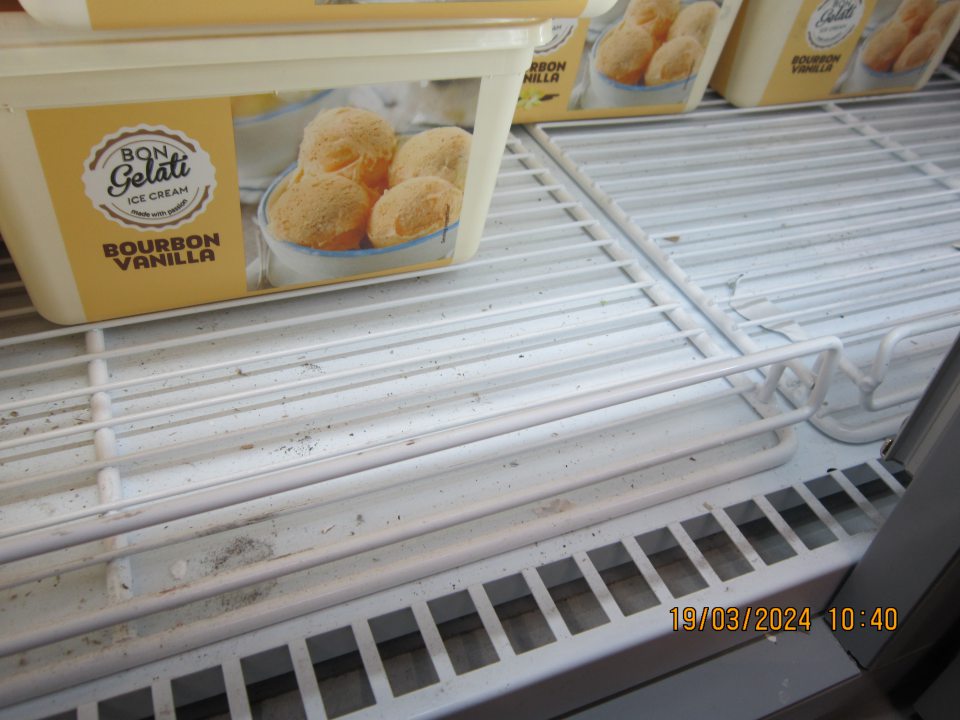 Prachom, organickými nečistotami a  zbytkami potravín  znečistená spodná časť pod mriežkami v  mraziacej vitríne na uchovávanie mrazených krémov na predajnej ploche.