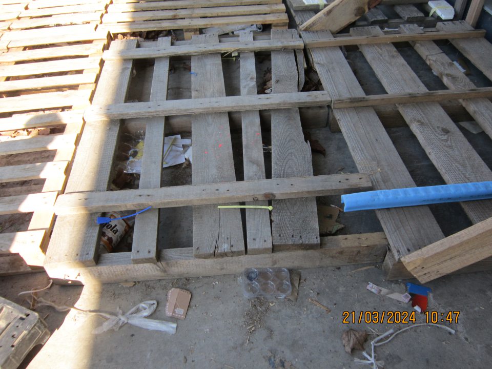 Hrubé nečistoty, kúsky kartónov, zbytky obalového materiálu, drevené  triesky pod paletami vo vonkajšom priestore prevádzkarne v blízkosti rampy pre príjem potravinového tovaru.