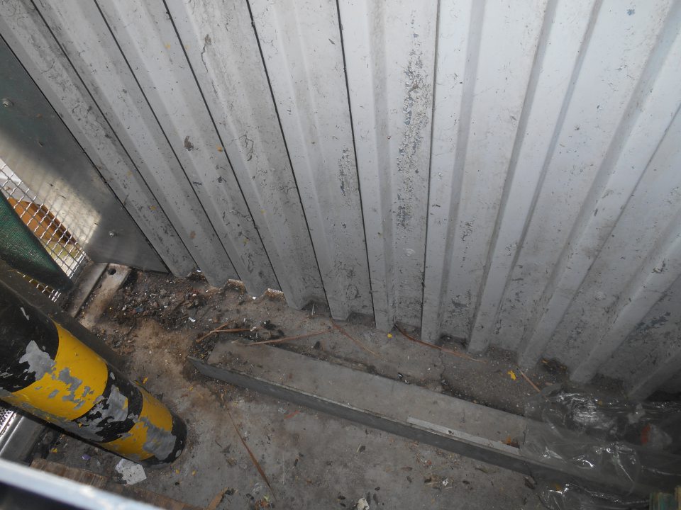 Znečistený priestor za prázdnymi drevenými paletami a vratnými obalmi pozdĺž obvodovej steny na rampe.