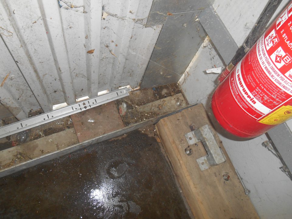 Znečistený priestor za prázdnymi drevenými paletami a vratnými obalmi pozdĺž obvodovej steny na rampe.