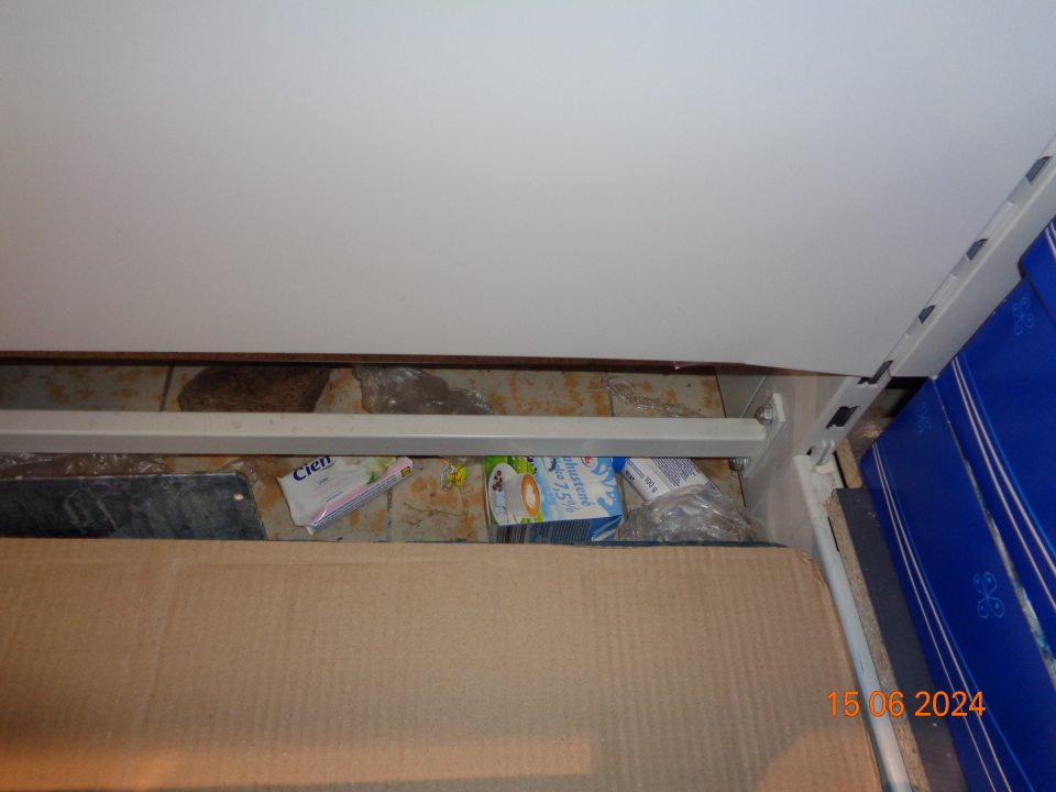 Znečistená podlaha prachom, kúskami plastov, plastovými vreckami, zbytkami organických nečistôt, spadnutým tovarom v priestore medzi paletami s trvanlivým mliekom a regálom s drogistickým tovarom na predajnej ploche.