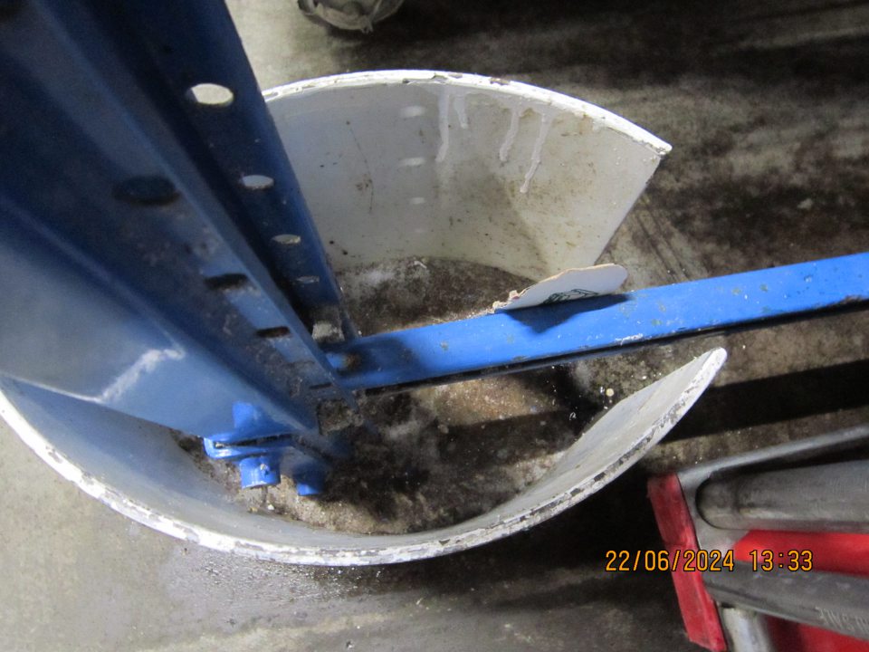 Znečistená podlaha v suchom sklade pri pätke stĺpu paletového regálu a v jeho okolí zaschnutou čiernou špinou a nahromadenou vrstvou prachu. 