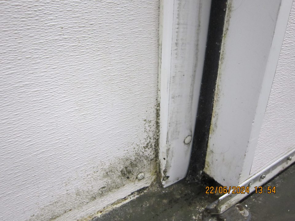 Znečistená podlaha a výskyt plesne na stene v blízkosti zaťahovacích dverí do chladiarenského boxu určeného k uchovávaniu mäsových výrobkov  v zázemí prevádzkarne.