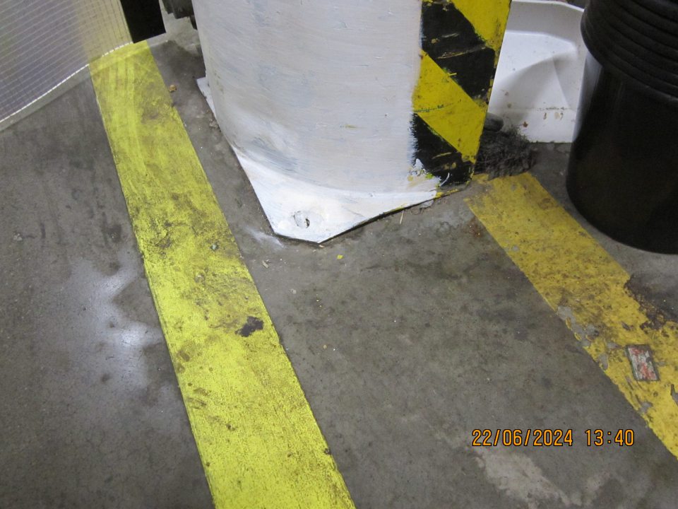 Znečistená podlaha v suchom sklade pri zábranách pred plastovými dverami vedúcimi do manipulačnej chodby smerujúcej k predajnej ploche.