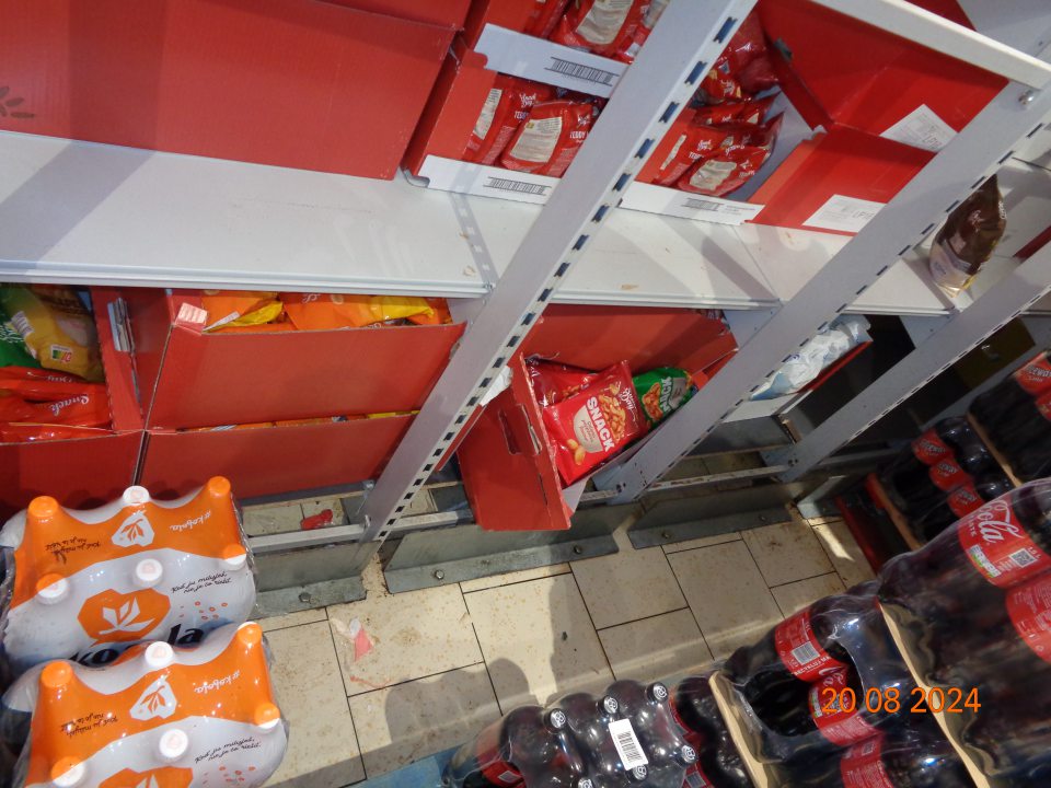 Na regáloch na uchovávanie trvanlivého slaného pečiva na predajnej ploche súvislá vrstva prachu a podlaha znečistená prachom, kúskami plastov a nánosmi špiny.