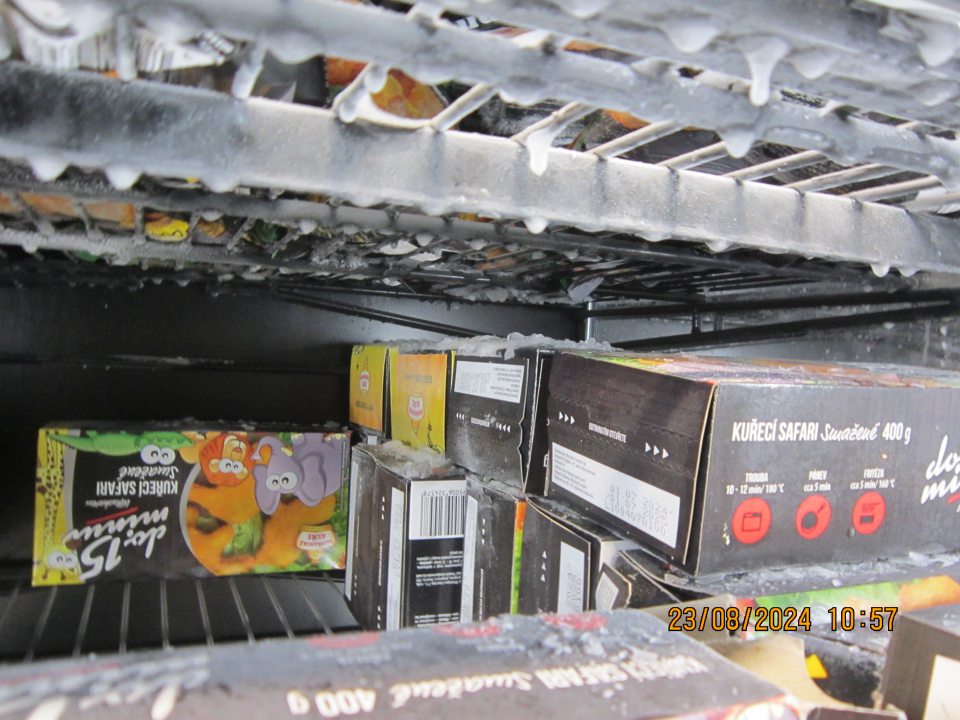 Zamrznuté kvapky vody na predeľovacích policových mriežkach a nadmerná námraza na kartónových baleniach znehodnoteného výrobku – hlbokozmrazený polotovar v poškodenom obale v mraziacej vitríne na predajnej ploche.