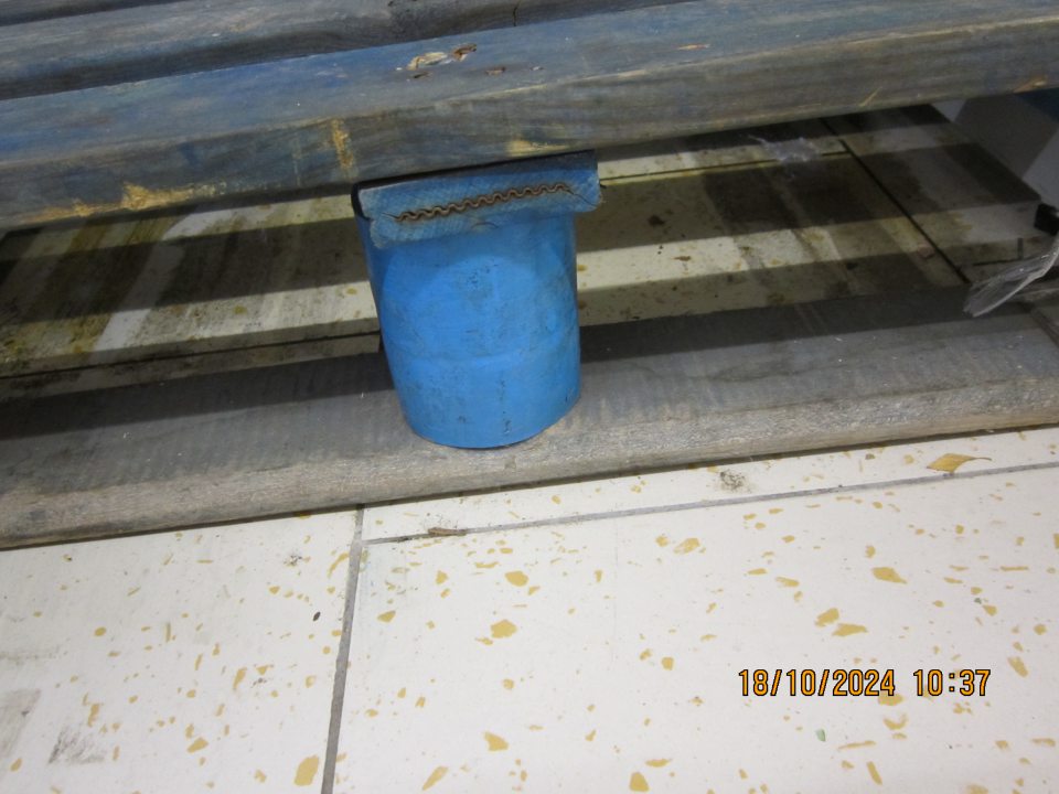 Podlaha na predajnej ploche pod paletami s minerálnymi vodami  znečistená prachom, kúskami plastov a vytečeným obsahom. 