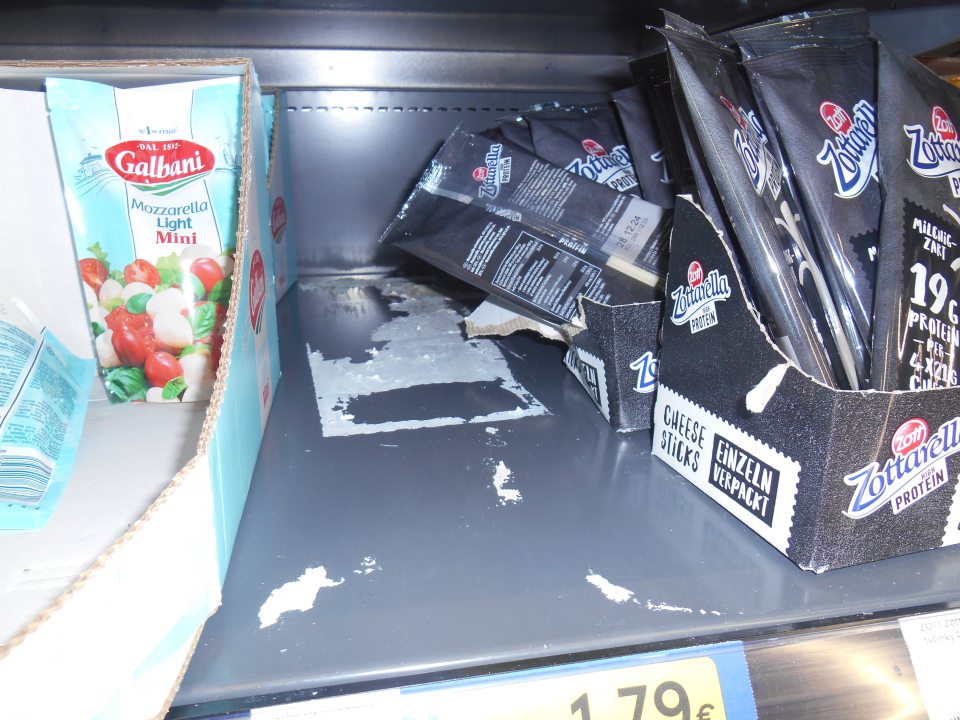 Úložná plocha v chladiarenskej vitríne na predajnej ploche znečistená nálepmi kartónových obalov.