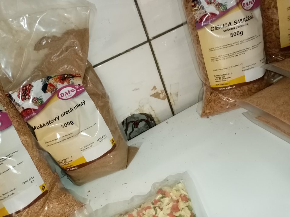 Porušená celistvosť steny za regálmi s koreninami (muškátový orech mletý, smažená cibuľa) v priestore sa nachádza neprekrytá kabeláž.