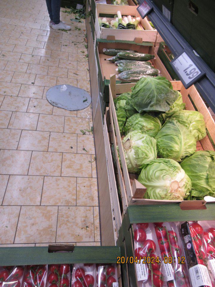 Znečistená podlaha na predajnej ploche v okolí zeleniny- zbytky zeleniny (najmä zelené časti zeleniny) a plechová podložka zo smetného koša.