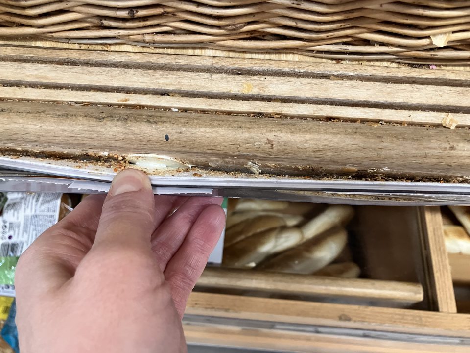 Predajná plocha - odlepené a znečistené cenovkové lišty od napadaných omrviniek na regáloch s nebaleným pečivom