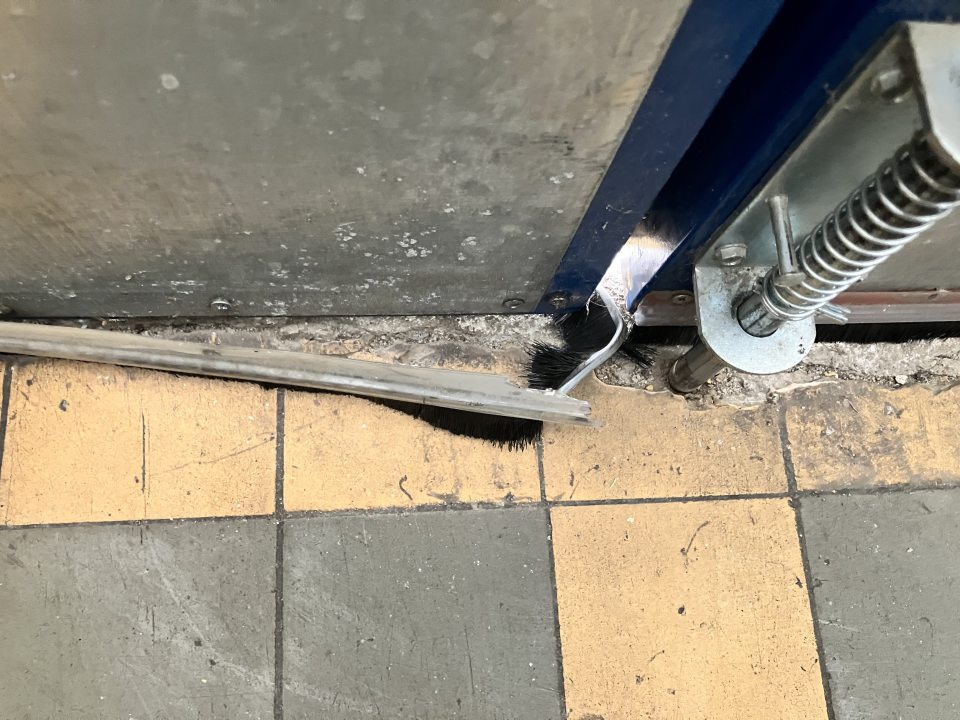 Poškodená podlaha a odtrhnuté tesnenie v príjmovej chodbe v zázemí predajne.