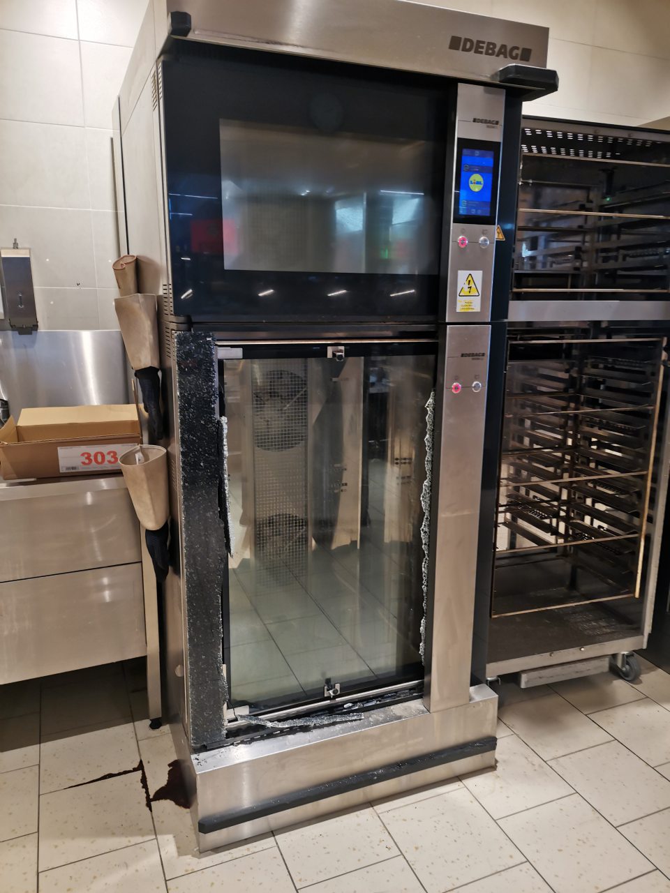 Poškodené sklo na spodných dverách technologického zariadenia slúžiaceho na dopekanie pekárenských výrobkov vyrábaných z mrazeného polotovaru.