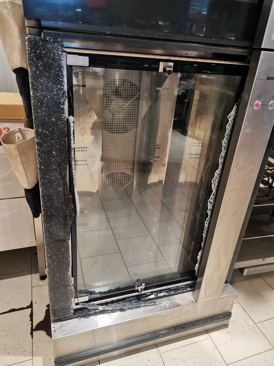 Poškodené sklo na spodných dverách technologického zariadenia slúžiaceho na dopekanie pekárenských výrobkov vyrábaných z mrazeného polotovaru.