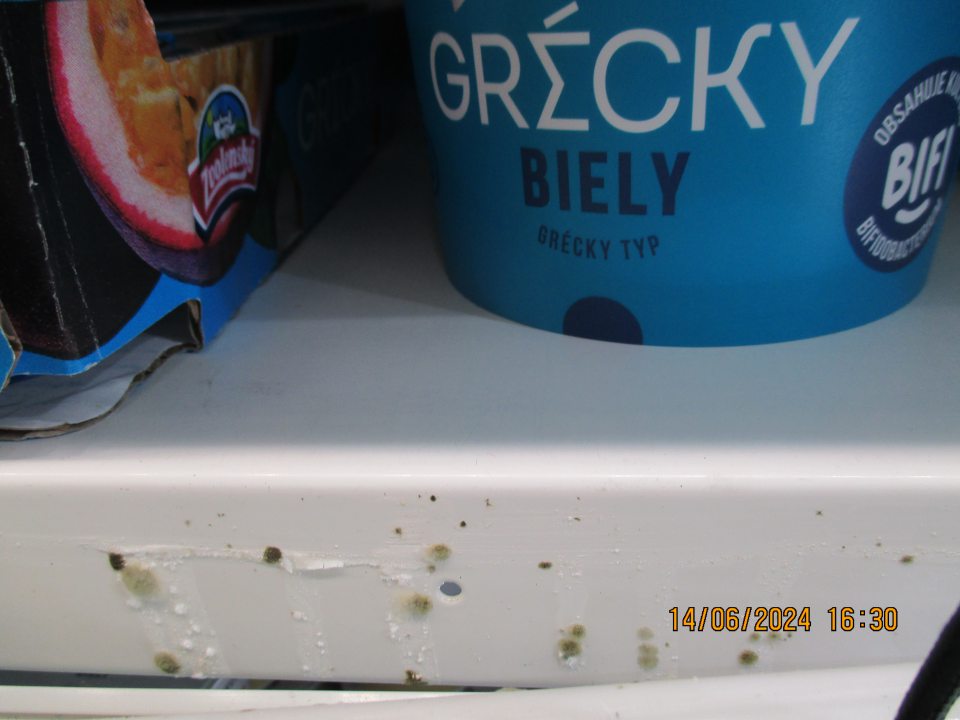 V chladiacej vitríne s uloženými mliečnymi výrobkami výskyt plesne na policiach zariadenia a vytečený obsah jogurtu na viacerých miestach.