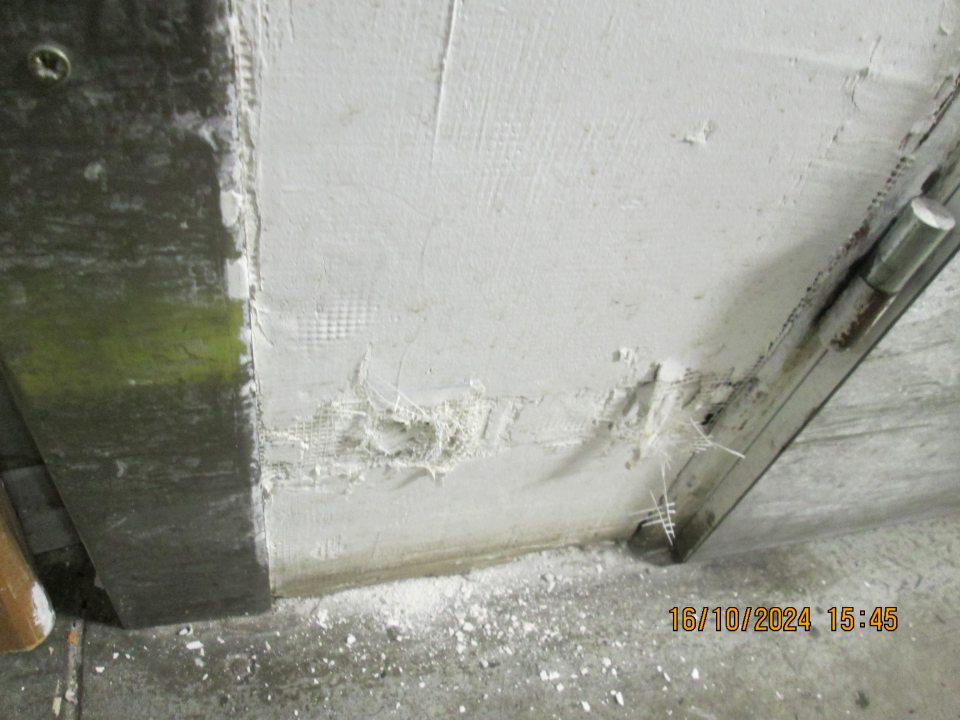 Stena v časti pred chladiacim boxom poškodená, zvyšky omietky na podlahe.