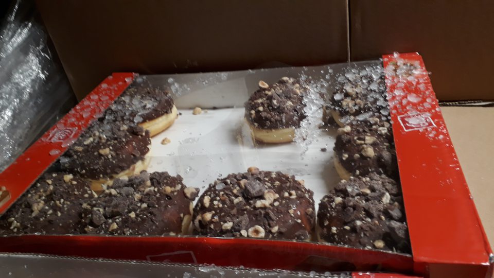 Pod agregátom v mraziacom boxe uložené hlbokozmrazené donuty v kartónoch s roztrhnutým celofánom a pokryté kúskami ľadu z agregátu.