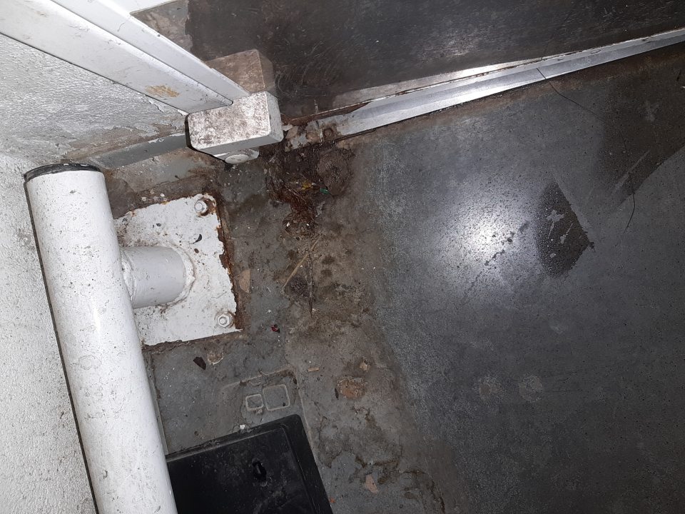 Znečistená podlaha v zázemí pri dverách do miestnosti na skladovanie sanitačných prostriedkov a zariadení.