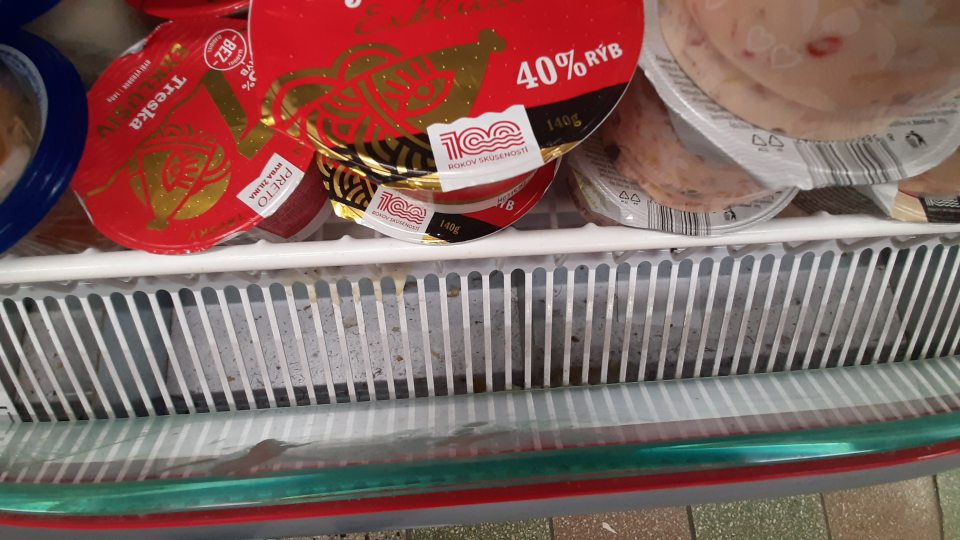 Znečistená chladiaca vitrína na mliečne výrobky na predajnej ploche v spodnej časti v mieste pod mriežkou prachom, zvyškami zaschnutých potravín a iných nečistôt.