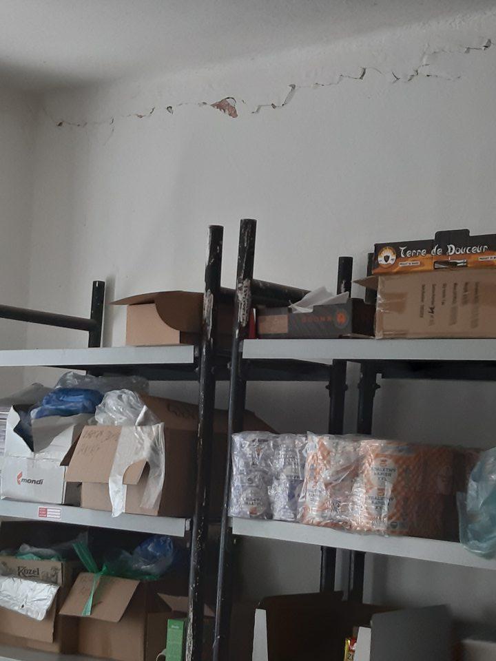 Stena v suchom sklade potravín nad regálmi, nad chladiacim zariadením má poškodenú omietku, ktorá miestami opadáva.