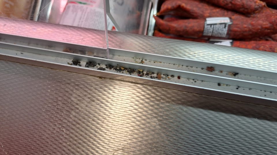 2. Znečistená chladiaca vitrína v drážkach posuvných dverí zbytkami potravín a rôznymi nečistotami v mieste predaja krájaných mäsových výrobkov.