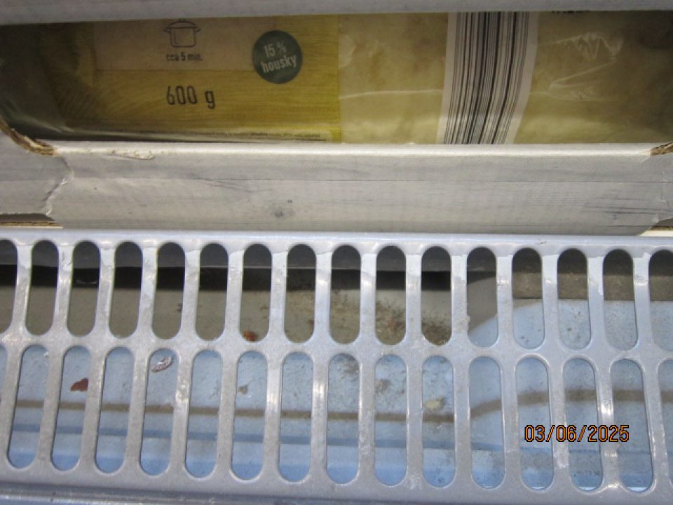 Pod kovovou mriežkou chladiacej vitríny pre mliečne výrobky sa nachádzajú nečistoty. 