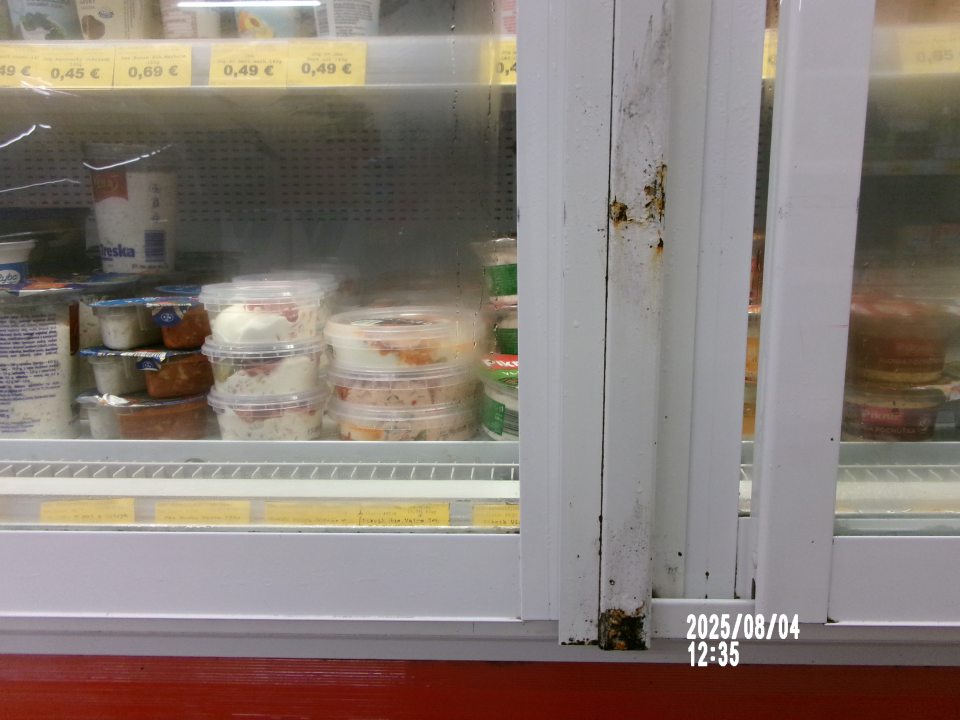 Skorodovaný rám posuvných dverí na chladiarenskej vitríne s uchovávanými mliečnymi výrobkami.