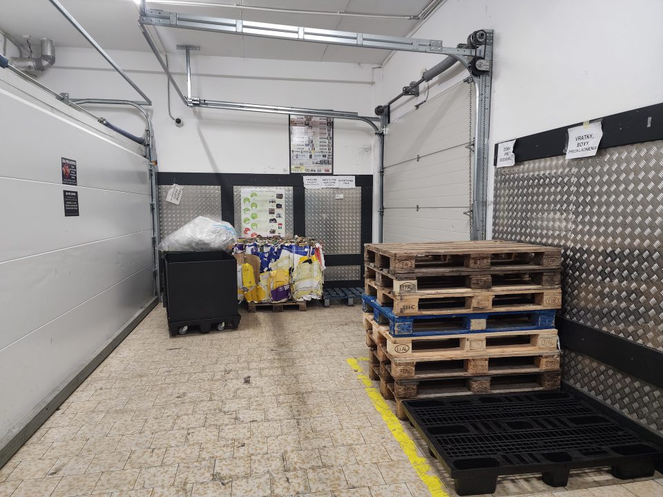 Znečistená príjmová časť, skladované zlisované kartóny v kocke, drevené palety, vratné plastové obaly.