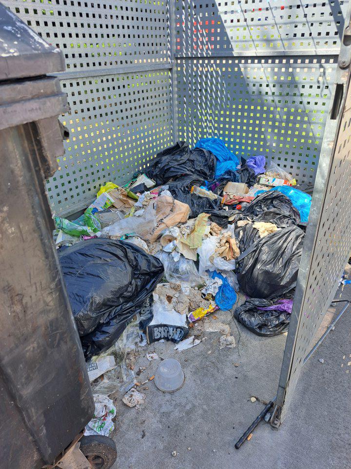 Vonkajšia kovová klietka na plastovú nádobu na smeti - v zlom hygienickom stave. Odpadky mimo smetnej nádoby.