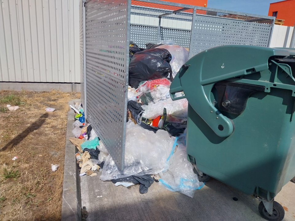 Rozsypané smeti mimo zbernej nádoby, stojisko kontajneru otvorené a plné smetí. Kontajner mimo stojiska.