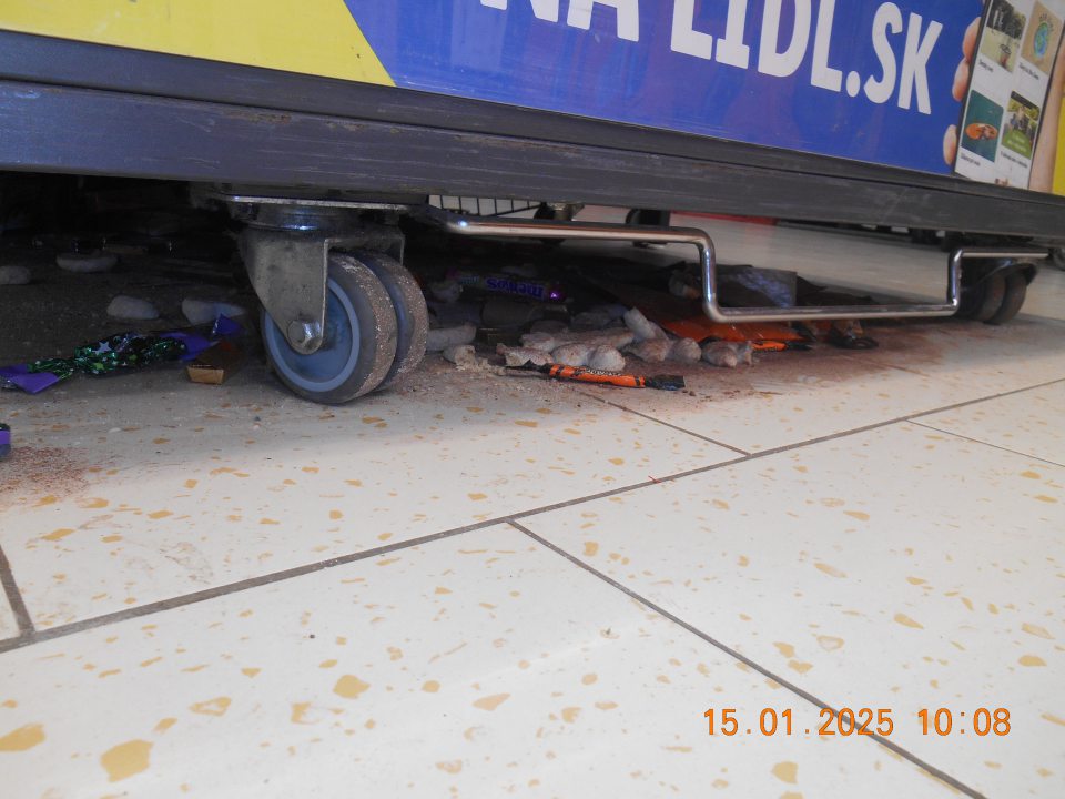 Na predajnej ploche pod prepravným košom na zľavnený tovar – celé kúsky a zbytky tuhých a vytečených tekutých potravín, kúsky obalových materiálov, rozsypané balenia cukroviniek, sypkého tovaru (kakao) a tovaru z regálu non food (ponožky, tričká).