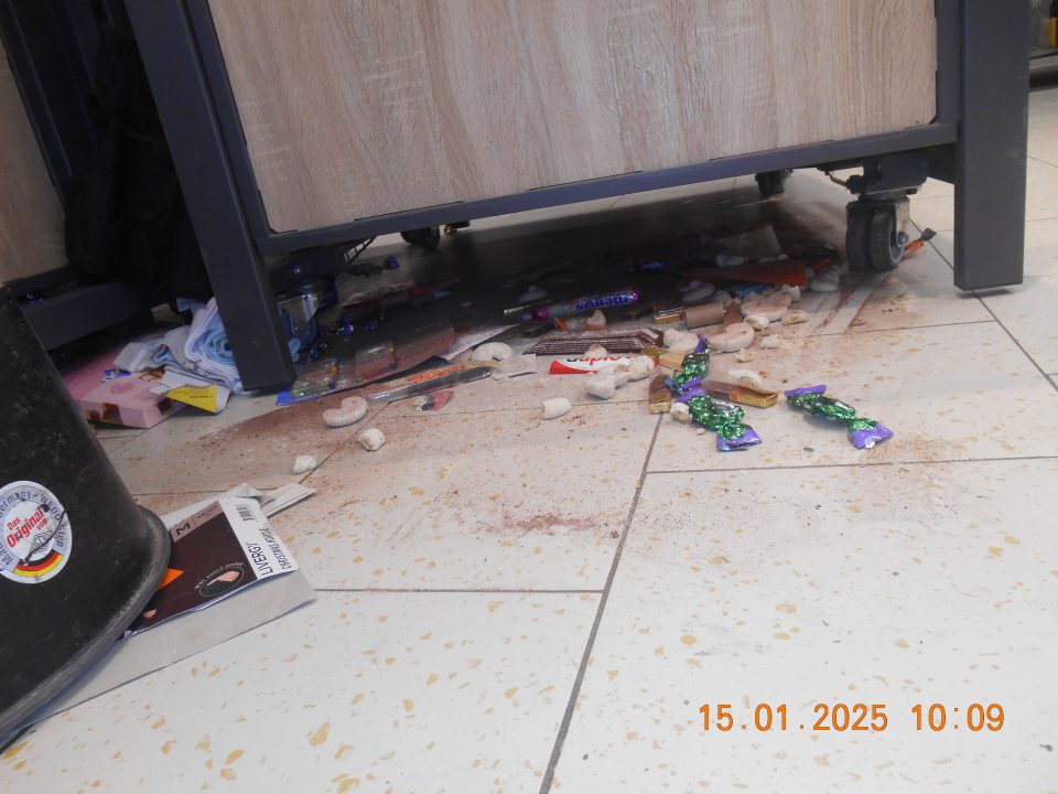 Na predajnej ploche pod prepravným košom na zľavnený tovar – celé kúsky a zbytky tuhých a vytečených tekutých potravín, kúsky obalových materiálov, rozsypané balenia cukroviniek, sypkého tovaru (kakao) a tovaru z regálu non food (ponožky, tričká).