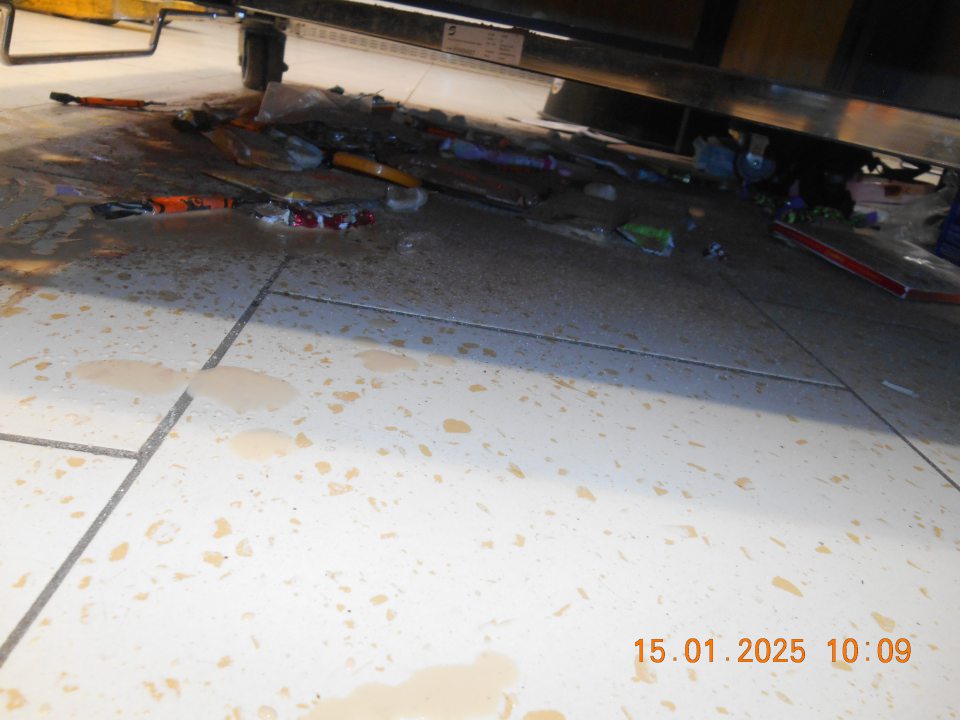 Na predajnej ploche pod prepravným košom na zľavnený tovar – celé kúsky a zbytky tuhých a vytečených tekutých potravín, kúsky obalových materiálov, rozsypané balenia cukroviniek, sypkého tovaru (kakao) a tovaru z regálu non food (ponožky, tričká).