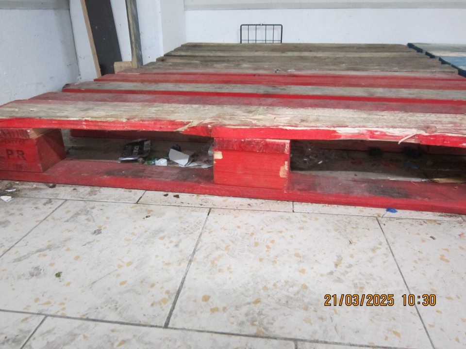 Podlaha znečistená nánosmi prachu a  zbytkami obalového materiálu pod paletami umiestnenými pri príjmovej rampe v zázemí prevádzky.