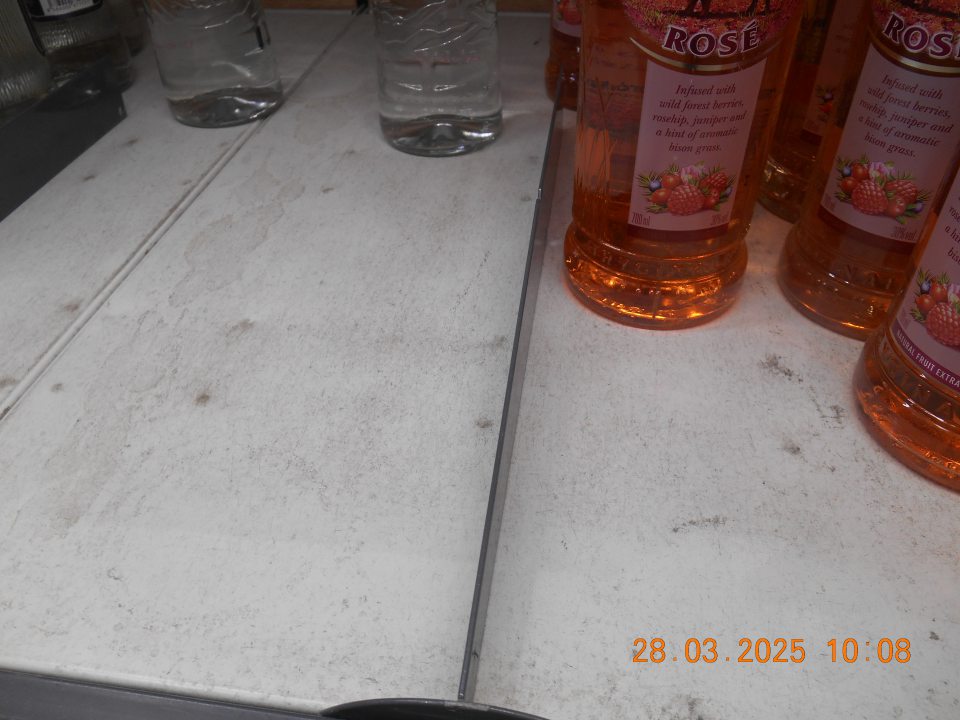 Regál na uchovávanie alkoholických nápojov na predajnej ploche prevádzky znečistený prachom a zaschnutou čiernou špinou.